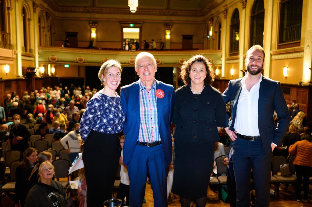 The moderator and the relieved and smiling three candidates with the hall in the background